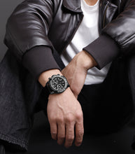 Load image into Gallery viewer, Person wearing a black leather jacket and watch, sitting against a dark background
